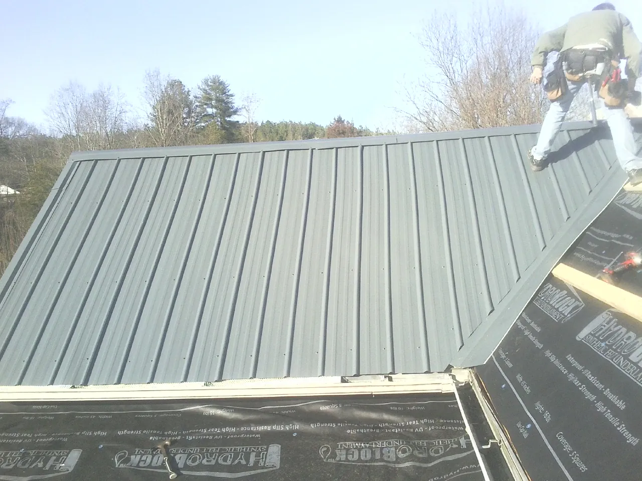 Crew installing dark green standing seam panels over synthetic underlayment in Carlisle